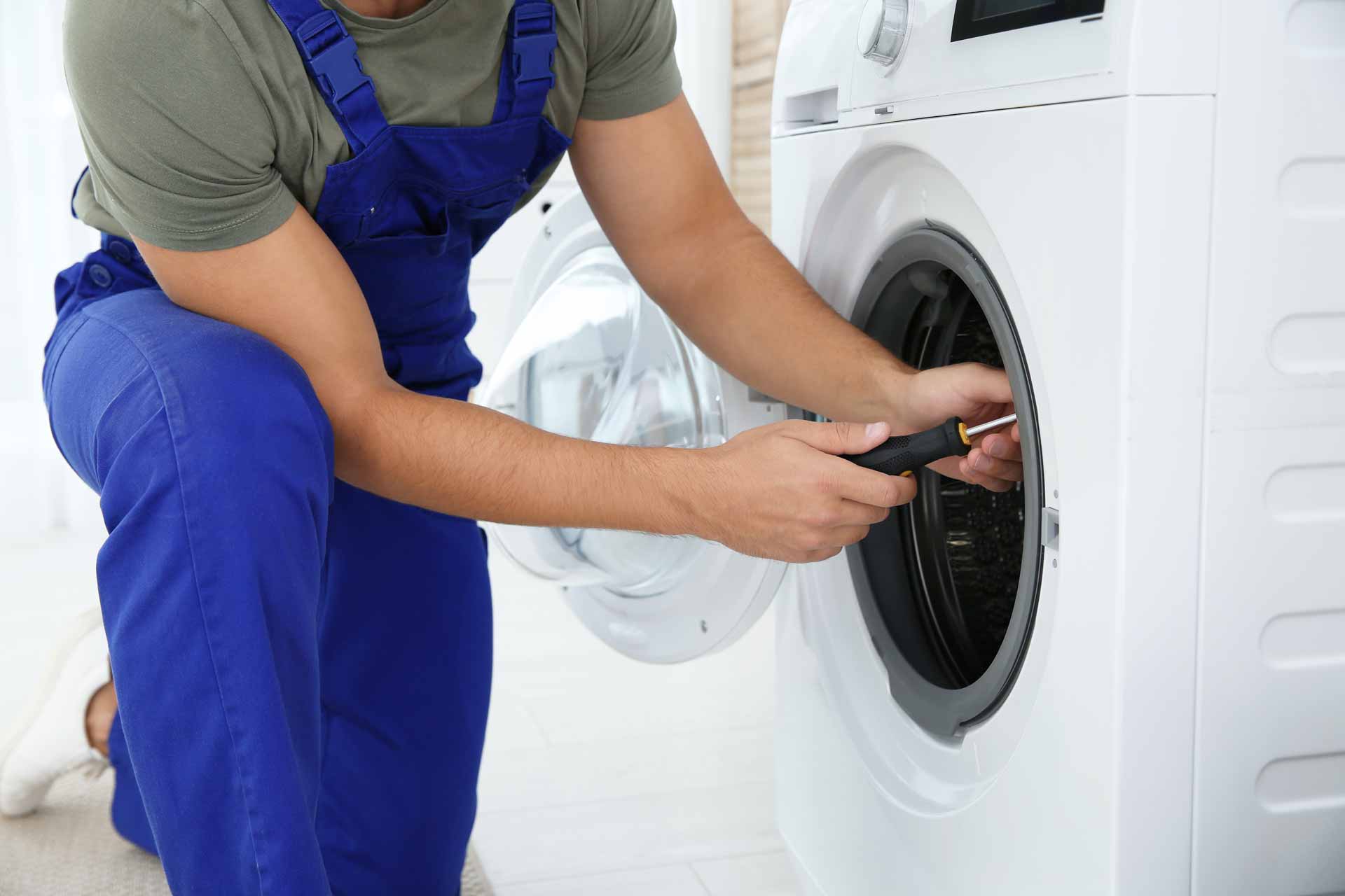 A technician in blue overalls repairing a washing machine