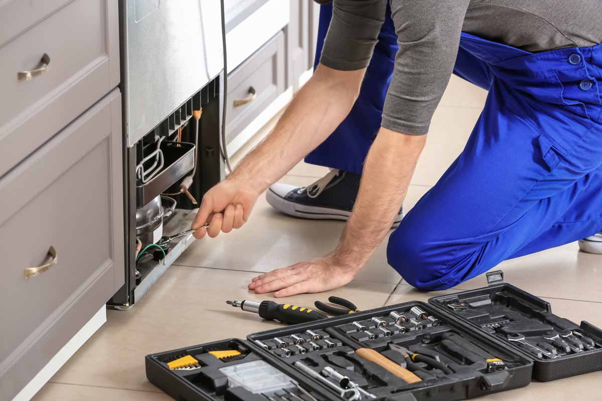 A technician kneeling to repair a refrigerator